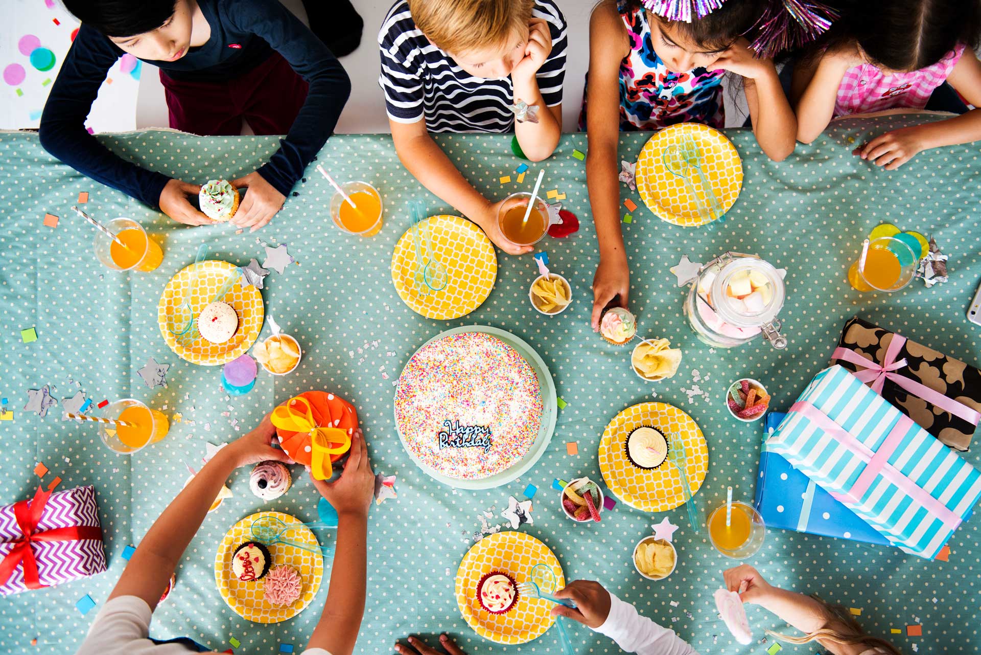 Birthday party table with kids, colorful plates, cake, and drinks. Featuring party supplies and decorations. Perfect for events and celebrations.