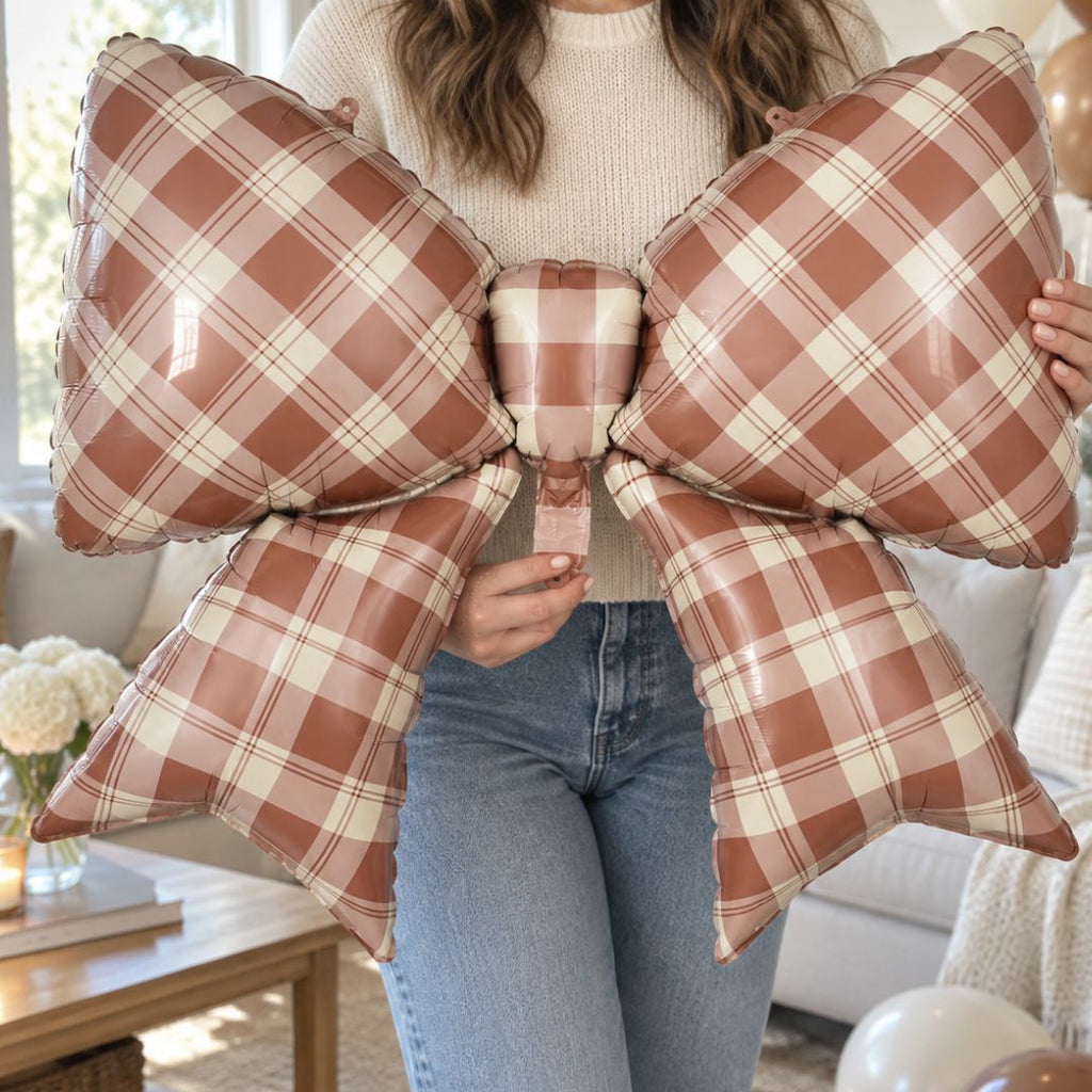 Party Paradise Store brown gingham plaid bow foil balloon held by a person for fall party decorations.
