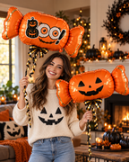 Party Paradise Store woman holding two orange Halloween candy balloons with Boo and jack-o-lantern faces in a home
