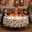 Children in costumes sitting at a round table with a Party Paradise Store Halloween table cover featuring ghost prints
