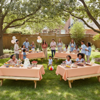 Party Paradise Store orange reusable plastic table covers on picnic tables at an outdoor garden party with guests.